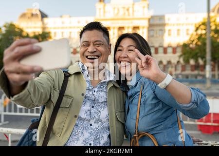 Couple d'âge mûr heureux prenant le selfie devant le bâtiment Banque D'Images