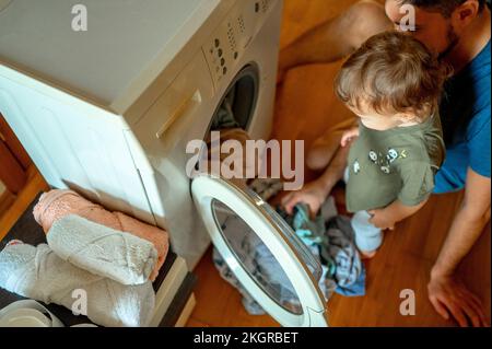 Fils avec père en train de charger les vêtements dans la machine à laver Banque D'Images