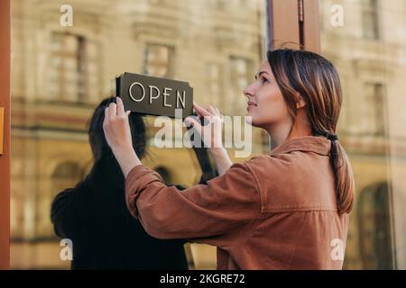 Jeune entrepreneur tenant une enseigne ouverte sur la porte en verre du café Banque D'Images