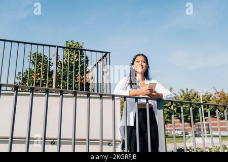 Jeune femme heureuse tenant un smartphone penché sur la rampe sous le ciel Banque D'Images