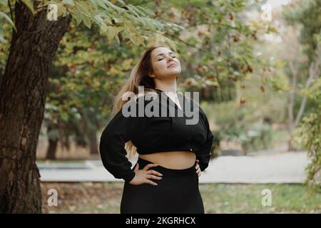 Jeune femme souriante debout avec les mains sur les hanches, respirant de l'air frais au parc Banque D'Images