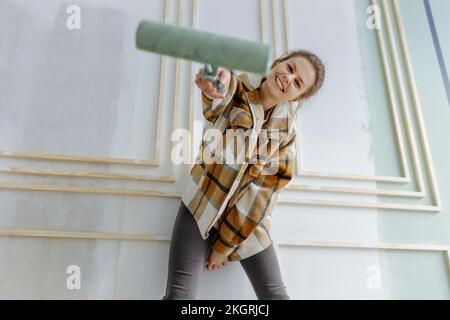 Femme souriante avec rouleau de peinture devant le mur à la maison Banque D'Images