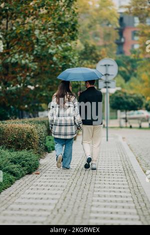 Jeune couple marchant ensemble sous un parapluie sur une piste de marche Banque D'Images