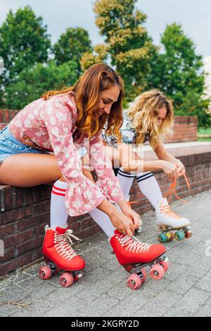 Femme souriante avec un ami nouant la dentelle des patins à roulettes Banque D'Images