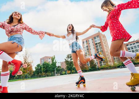 Des amis heureux tenant les mains pratiquant le patinage à roulettes sur le terrain de sport Banque D'Images