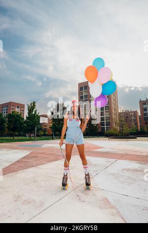 Femme portant des patins à roulettes tenant des ballons colorés sur le terrain de sport Banque D'Images