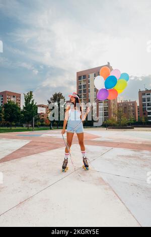 Jeune femme portant des patins à roulettes tenant des ballons colorés sur le terrain de sport Banque D'Images