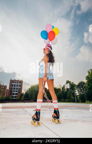 Femme souriante portant des patins à roulettes tenant des ballons colorés sur le terrain de sport Banque D'Images