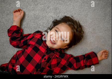 Joli petit garçon dans une chemise à carreaux couchée sur un tapis Banque D'Images