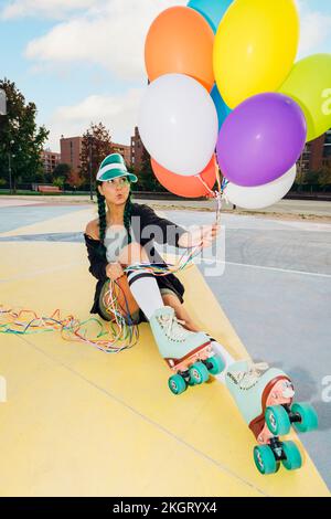 Femme portant des patins à roulettes tenant des ballons colorés sur le terrain de sport Banque D'Images