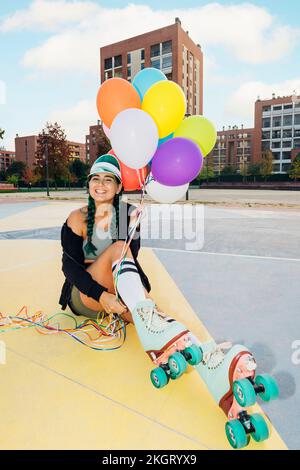 Une femme heureuse portant des patins à roulettes tenant des ballons colorés sur le terrain de sport Banque D'Images