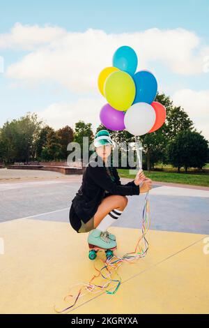 Jeune femme portant des patins à roulettes qui se croupe et tient des ballons colorés sur le terrain de sport Banque D'Images