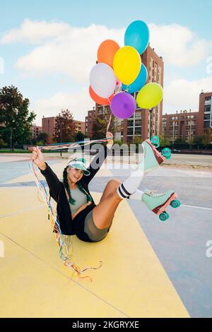 Jeune femme heureuse portant des patins à roulettes tenant des ballons colorés sur le terrain de sport Banque D'Images