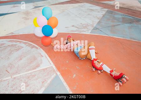 Femme souriante portant des patins à roulettes portant des ballons colorés couchés sur un terrain de sport Banque D'Images