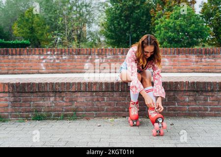 Femme souriante laçage du patin à roulettes sur le mur Banque D'Images