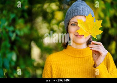 Femme souriante tenant la feuille d'érable jaune sur le visage Banque D'Images