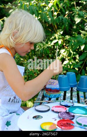 Petite fille peinture pots de fleurs dans le jardin Banque D'Images