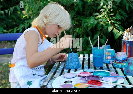 Petite fille peinture pots de fleurs dans le jardin Banque D'Images