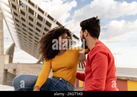 Jeune femme souriante assise avec un petit ami dans un ciel nuageux Banque D'Images