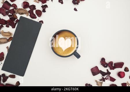 Cappuccino café décoré de mousse de lait à l'intérieur d'une tasse noire sur fond blanc et feuilles rouges Banque D'Images