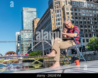 Grande / petite entreprise détendu homme mature assis à l'extérieur sur son bureau de péniche houseboat travaillant à la maison sur son ordinateur portable Canary Wharf Londres E14 Banque D'Images