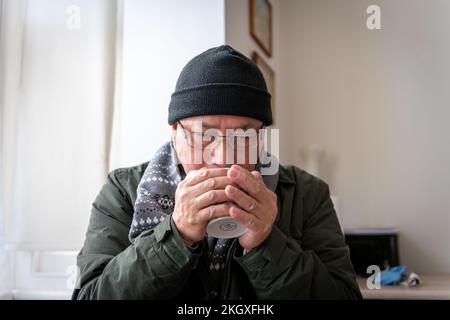 Un homme âgé qui essaie de rester au chaud à l'intérieur alors que le coût de l'énergie domestique a plus que doublé. Banque D'Images