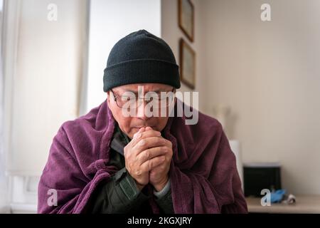 Un homme âgé qui essaie de rester au chaud à l'intérieur alors que le coût de l'énergie domestique a plus que doublé. Banque D'Images