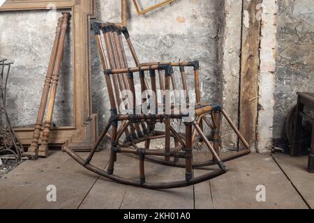 Un vieux fauteuil à bascule en bambou se tient dans une pièce sale, à l'ancien étage à côté d'autres choses anciennes Banque D'Images