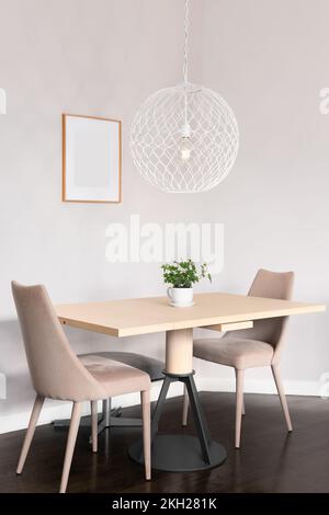 Une petite salle à manger confortable avec une table en bois sous une lumière suspendue blanche. Banque D'Images