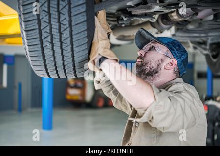 Contrôle de sécurité de la suspension de véhicule par un mécanicien automobile professionnel de race blanche. Thème d'entretien du véhicule. Banque D'Images