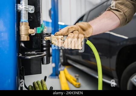 Gros plan du mécanicien qui branche un tuyau sur l'outil de compresseur d'air de roue fixe installé dans un atelier de voiture professionnelle. Banque D'Images