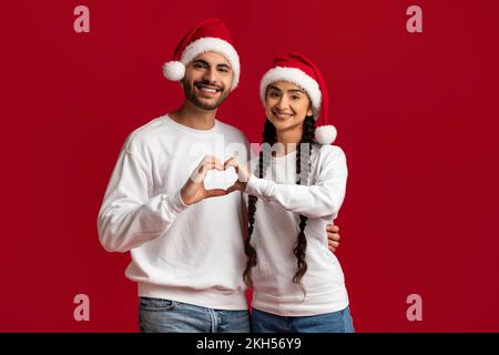 Couple arabe aimant à Santa Hats faisant le symbole de coeur avec leurs mains Banque D'Images