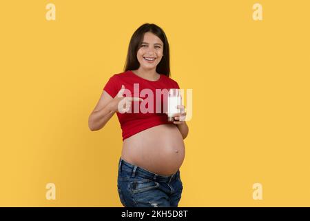 Bonne jeune femme enceinte pointant vers un verre de lait en main Banque D'Images