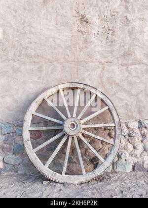 Un cliché vertical d'une ancienne roue de chariot en bois sur un fond d'un demi-mur de pavés Banque D'Images