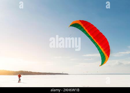 Vue panoramique de beaucoup de gens amis aiment faire du kite surf planche en costume chaud lors de la journée d'hiver ensoleillée et lumineuse à la surface enneigée du lac gelé Banque D'Images