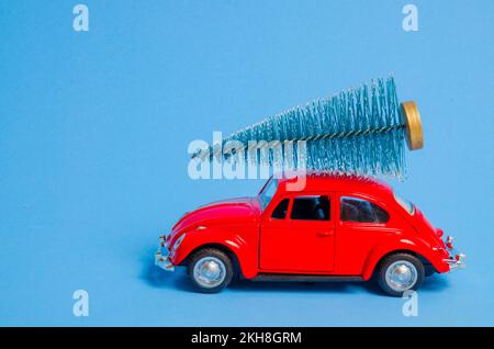 Londres, Angleterre - 24 novembre 2022: Voiture de jouet rouge et arbre de Noël sur le toit sur fond bleu. Voiture de jouet rouge vintage avec un petit arbre de Noël sur le toit Banque D'Images