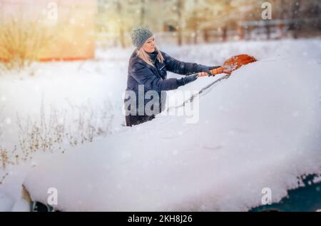 Une femme nettoie la voiture de la neige avec un balai en hiver Banque D'Images
