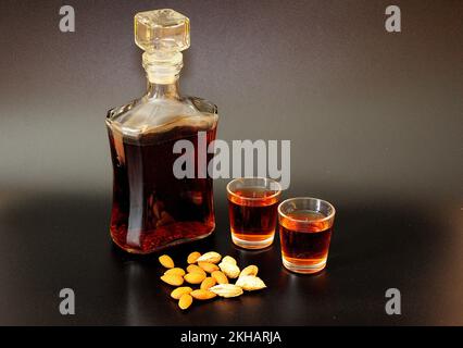 Amaretto, liqueur traditionnelle italienne à base d'amandes sur fond noir, à côté d'une poignée de noix. Gros plan. Banque D'Images