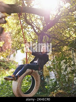 Des journées d'été insouciantes d'une enfance idyllique. Un préadolescent balançant sur une balançoire de pneu dans le jardin. Banque D'Images