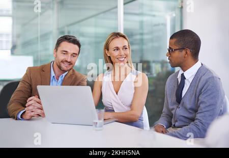 Satisfait de leurs résultats. un groupe diversifié de collègues utilisant un ordinateur portable au travail. Banque D'Images