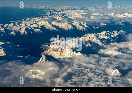 Vue aérienne des sommets enneigés des montagnes couverts de nuages, vue depuis la fenêtre de l'avion. Banque D'Images
