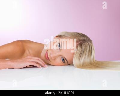 Belle peau et cheveux sains. Une courte photo en studio d'une belle jeune femme couché sur un fond rose. Banque D'Images