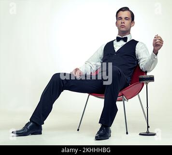 Une vie de loisirs. Portrait en studio d'un jeune homme élégant fumant une cigarette dans un cadre vintage. Banque D'Images