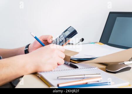 L'homme d'affaires utilisant une calculatrice et un ordinateur pour noter les données sur le bloc-notes - le concept de la finance Banque D'Images