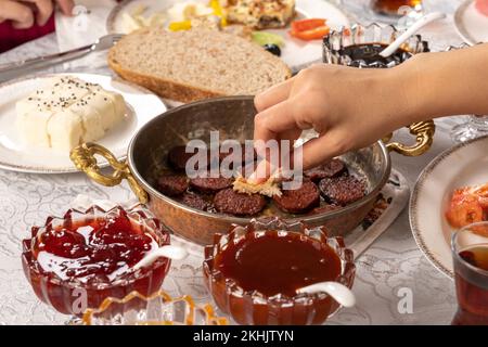 Gros plan de la femme qui coupe du pain à la main. Saucisse appelée dans le sucuk turc. Table de petit-déjeuner traditionnelle turque. Une femme de race blanche appréciant sa nourriture. Banque D'Images