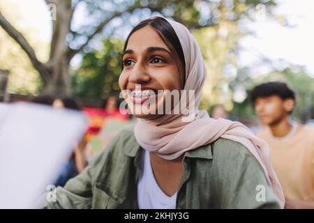 Une jeune fille musulmane souriant avec joie lorsqu'elle est assise avec un groupe de manifestants lors d'une manifestation contre le climat. Des jeunes activistes multiculturels rejoignant le climat mondial Banque D'Images