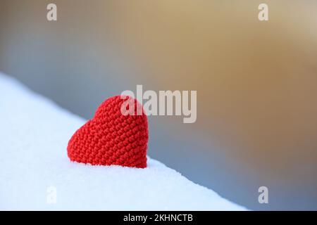 Coeur tricoté rouge dans la neige sur fond flou. Symbole de l'amour romantique, carte de Saint-Valentin Banque D'Images