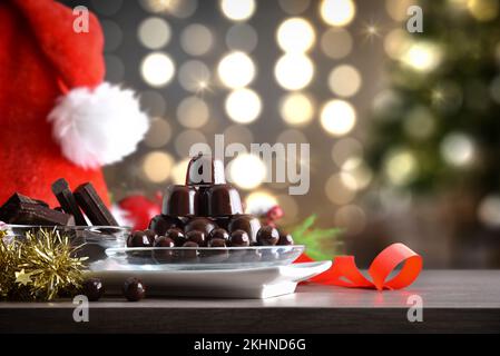 Assiette avec pile de chocolats et boules de chocolat noir sur table en bois avec décoration de Noël et fond de noël avec lumières. Vue avant. Banque D'Images