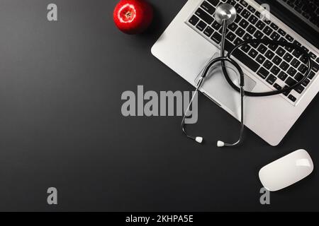 Ordinateur portable sur un bureau noir avec une pomme rouge sur la table et un stéthoscope pour un médecin travaillant sur les réseaux sociaux. Vue de dessus. Photo de haute qualité Banque D'Images