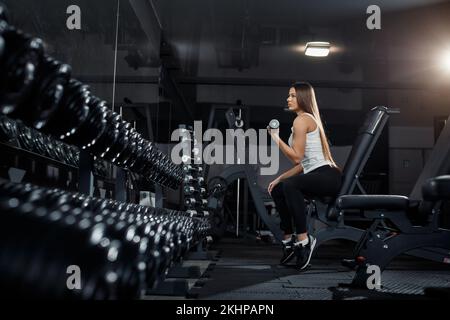 Mince, bodybuilder fille, soulève lourd haltère debout devant le miroir pendant l'entraînement dans la salle de gym. Concept sportif, combustion de graisse et une vie saine Banque D'Images